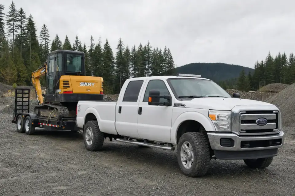 Yellow SANY SY60C excavator secured on a trailer behind a white 2013–2016 Ford F-350 Super Duty XLT crew cab